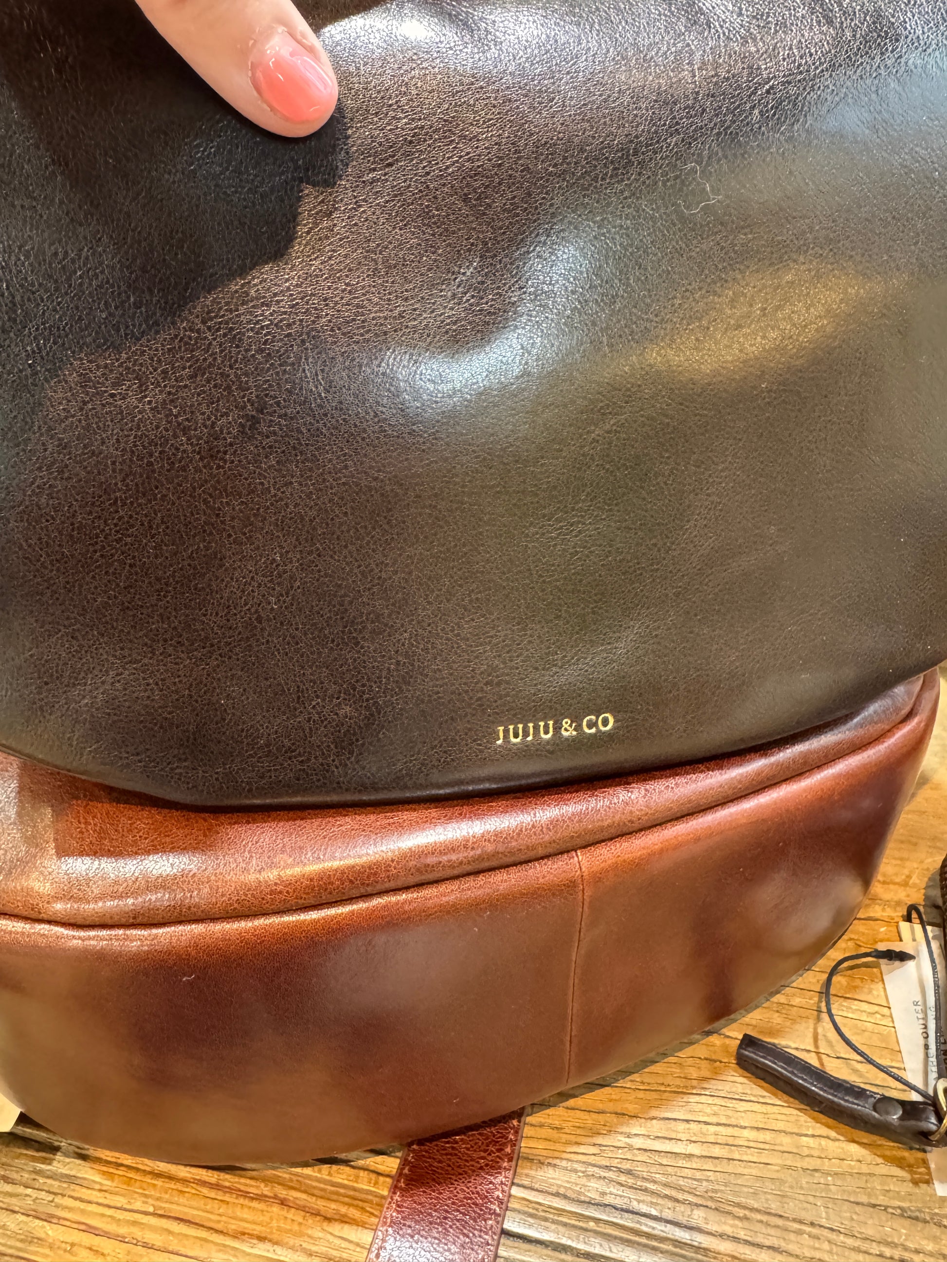 Brown leather bag with 'JUJU & CO' branding on a wooden surface.